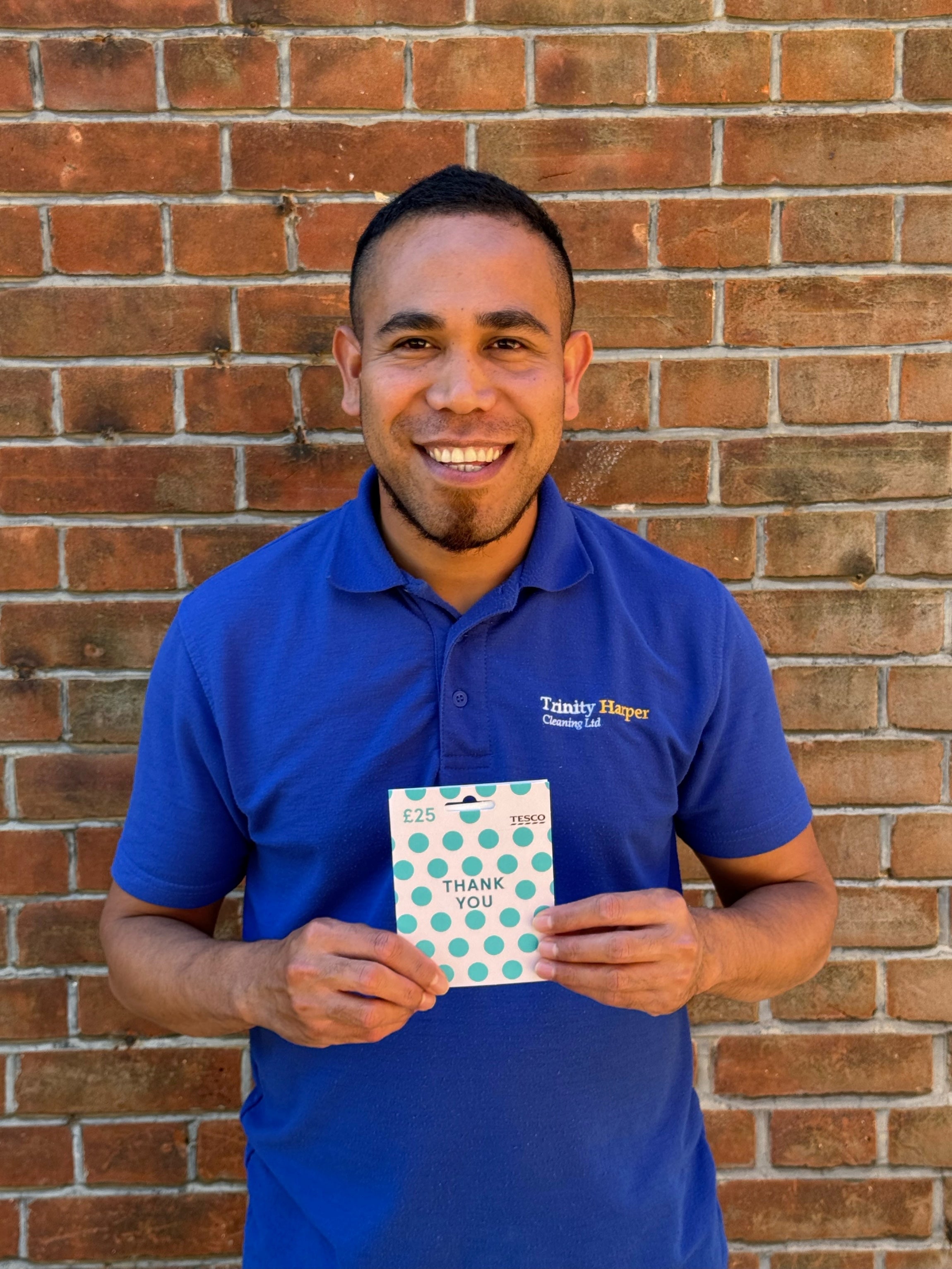 Man in blue shirt stood against a brick wall holding a gift card
