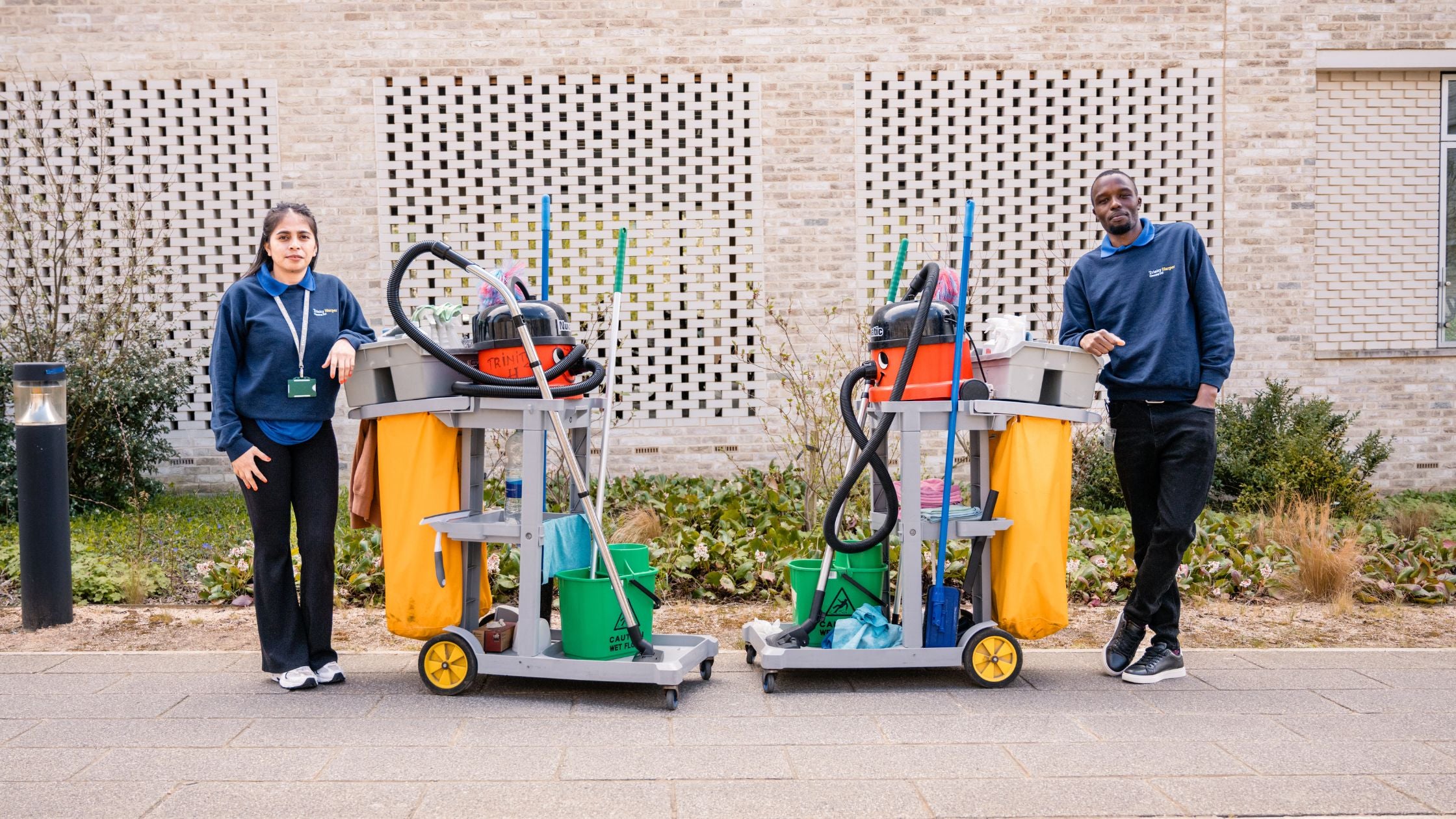Image of male and female cleaners in blue work clothes leaning against their cleaning trolleys