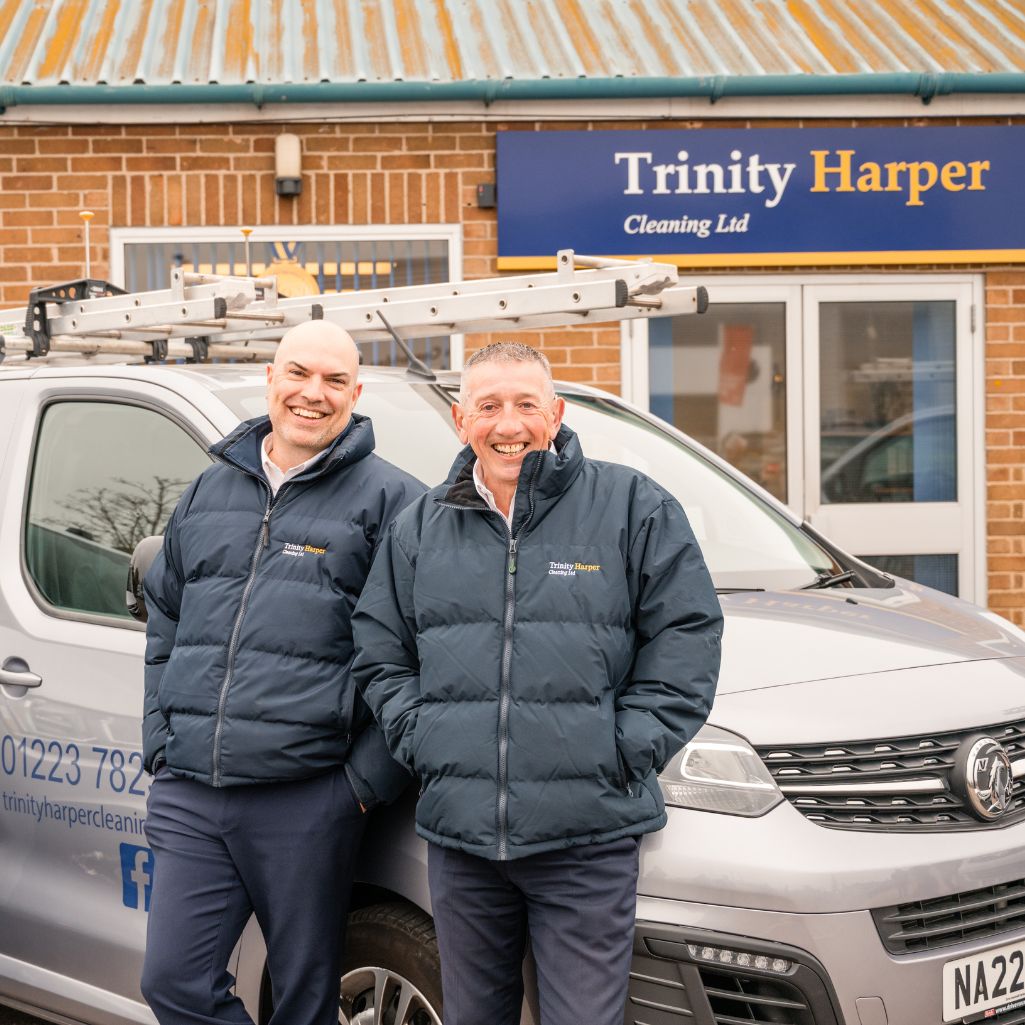 Picture of two men leaning against a silver van outside of Trinity Harper building