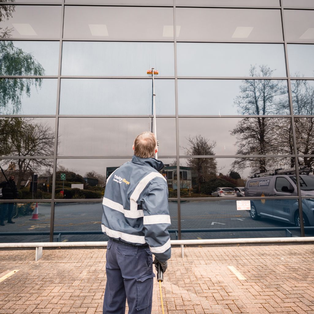 Image of man cleaning windows of a building with extended pole