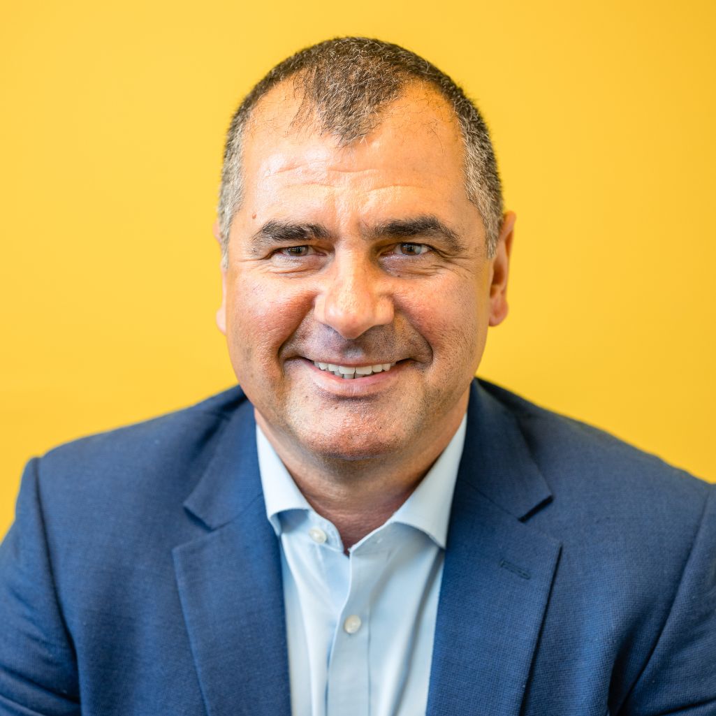 Close up of a smiling man in a blue jacket on a yellow background