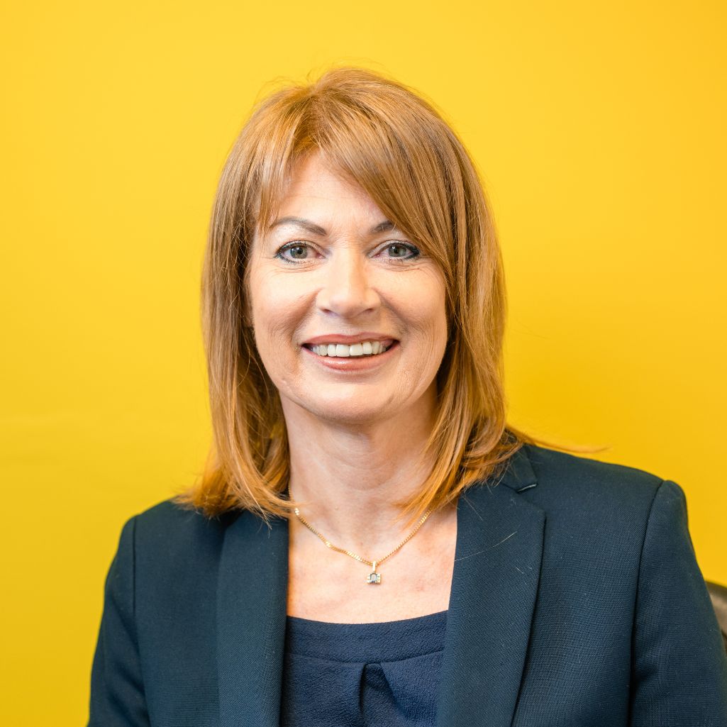 Picture of smiling lady in a blue suit with a yellow background