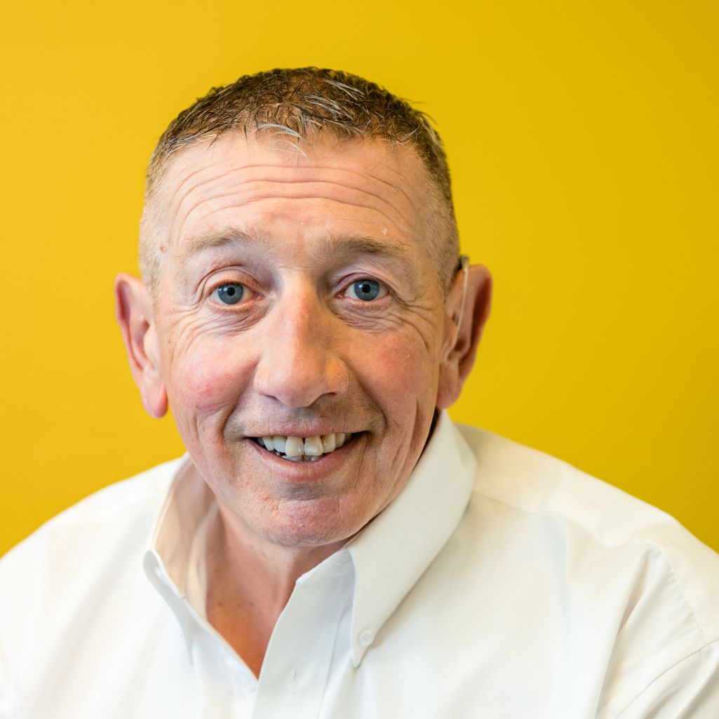 Close up of a man with blue eyes in a white shirt with a yellow background